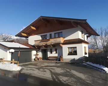 A modern house in Alpine style with a large balcony. It is situated in a snow-covered environment under a clear sky.
