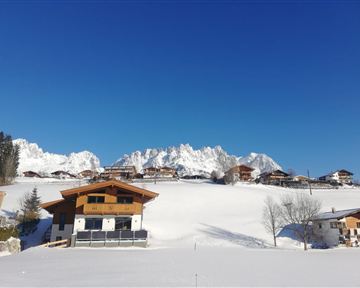 A picturesque winter landscape with snow-covered hills and majestic mountains in the background. The clear blue sky complements the tranquil atmosphere.