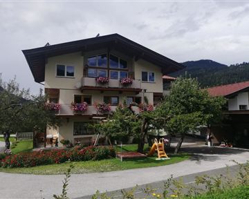 Ein charmantes Gebäude mit blühenden Balkonkästen. Im Vordergrund sind Blumenbeete und ein Spielplatz zu sehen.