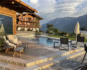 Eine luxuriöse Terrasse mit einem Pool und bequemen Sitzmöglichkeiten. Im Hintergrund sind majestätische Berge und eine malerische Landschaft zu sehen.