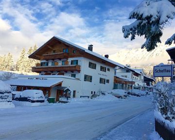 A snowy street with several houses in a winter village. The surroundings are picturesque with snow-covered trees and a clear sky.