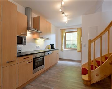 Eine moderne Küche mit Holzschränken und Edelstahlgeräten. Eine Treppe führt zu einem oberen Stockwerk.