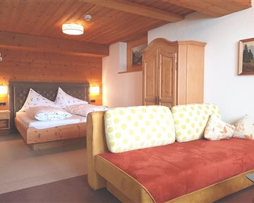A cozy bedroom with a double bed and a wooden wardrobe. A comfortable couch with colorful cushions complements the inviting atmosphere.