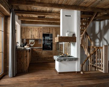 Ein gemütliches Holzhaus mit offener Küche und Treppe. Der Raum ist hell und modern gestaltet, mit warmen Holztönen.