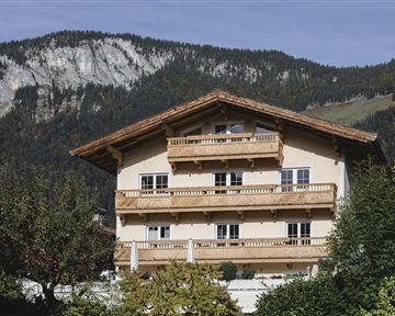 A charming house in alpine style with wooden decorations. In the background, majestic mountains and green terrain can be seen.