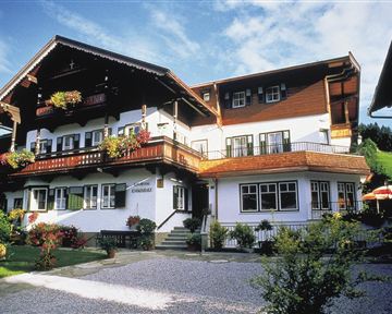 Ein charmantes, traditionelles Holzhaus mit blühenden Balkonblumen. Der grüne Garten und der blaue Himmel verleihen der Umgebung eine einladende Atmosphäre.