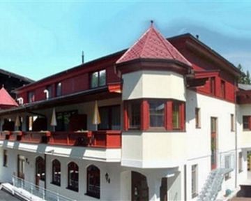 A charming building in alpine style with red and white elements. The facade has many windows and an attractive balcony.