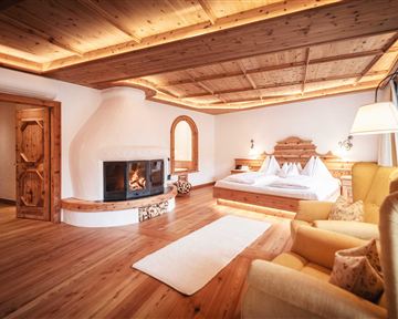 A cozy room with a large bed and a beautiful fireplace. Wood paneling and a soft carpet create a warm atmosphere.