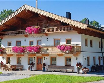 Ein traditionelles alpenländisches Haus mit schönen Balkonen und blühenden Pflanzen. Die Umgebung ist grün und sonnig, ideal für eine gemütliche Auszeit.