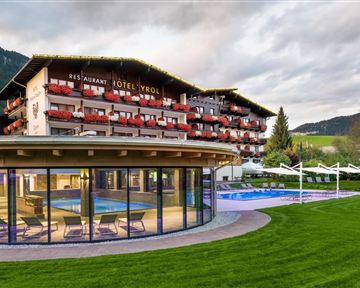 Ein modernes Hotel mit einem schönen Außenpool und gepflegtem Garten. Im Hintergrund sind die Berge und ein bewölkter Himmel zu sehen.