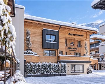 A cozy apartment building in winter, surrounded by fresh, fallen snow. The wooden facade gives it an inviting charm.